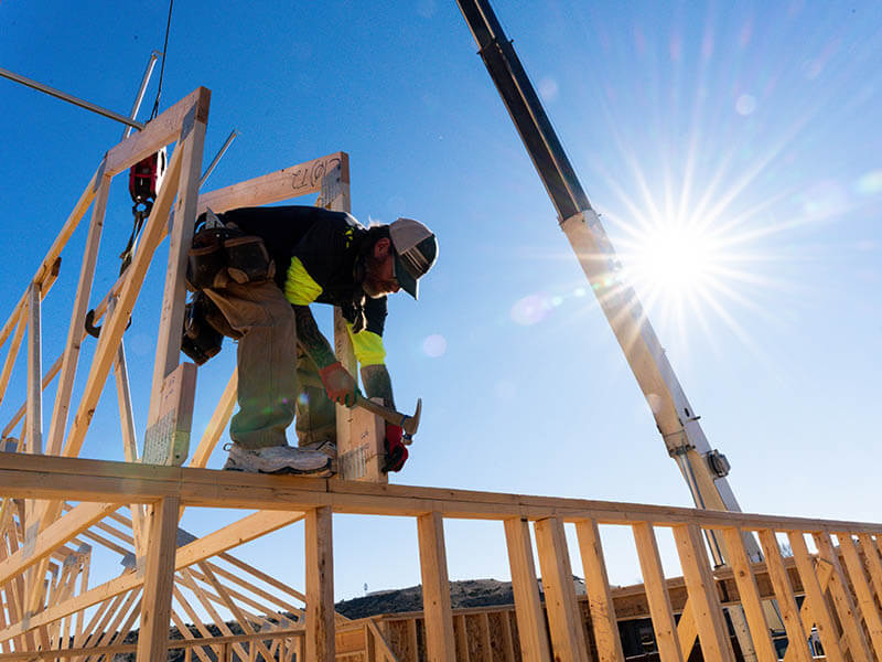 Framer nailing support structure while standing on a stud wall in residential construction.