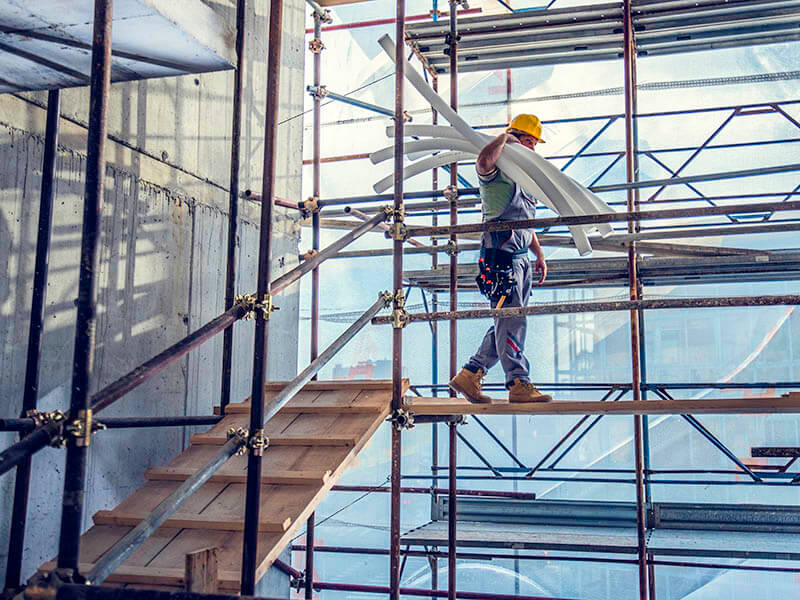 Construction worker carrying pipes.