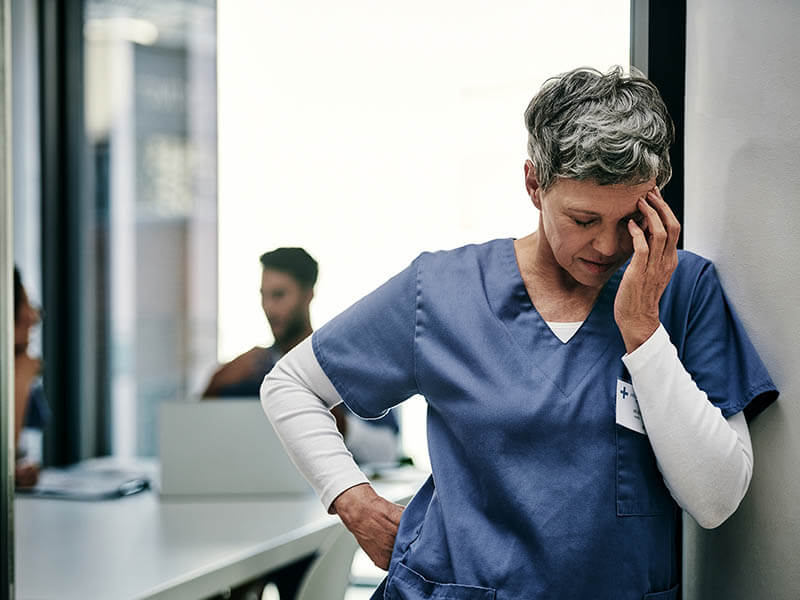 Nurse with her hand to her head leaning over.